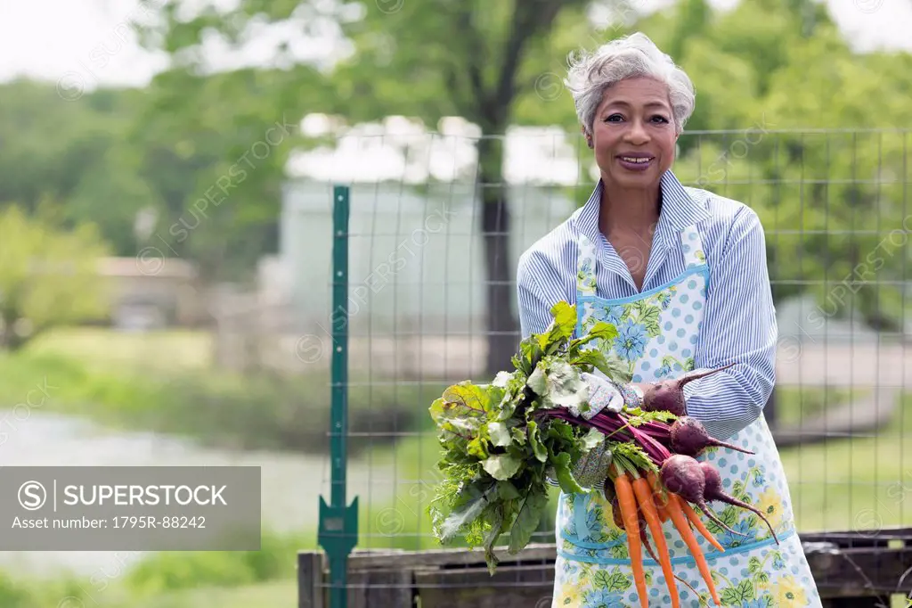 Portrait of senior woman holding carrots and beetroot
