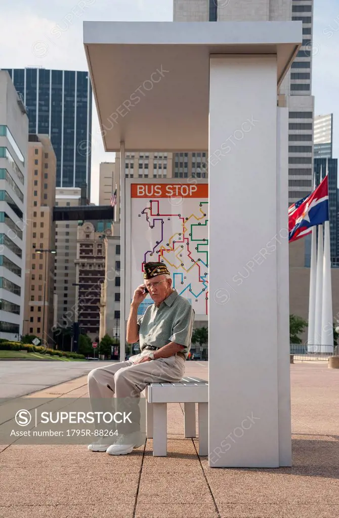 Senior man sitting at bus stop and using mobile phone