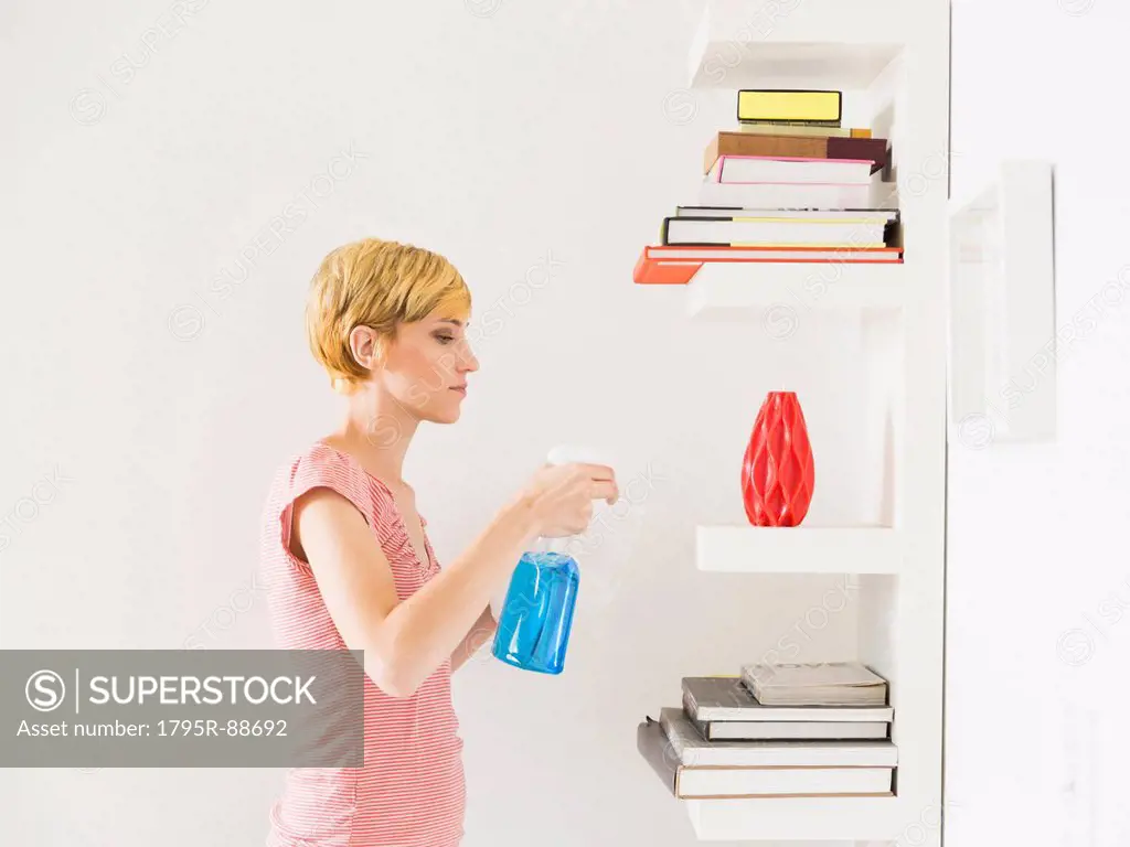 Young woman cleaning bookshelf