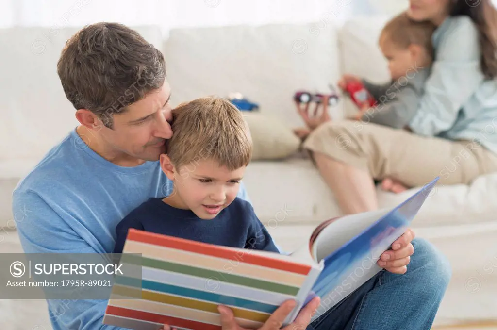 Parents with kids (12-17 months, 6-7) at home, father reading to son