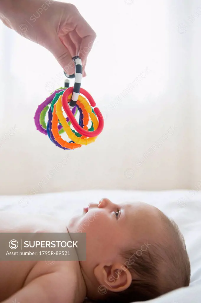 Hand holding colorful toy above baby girl (2-5 months)