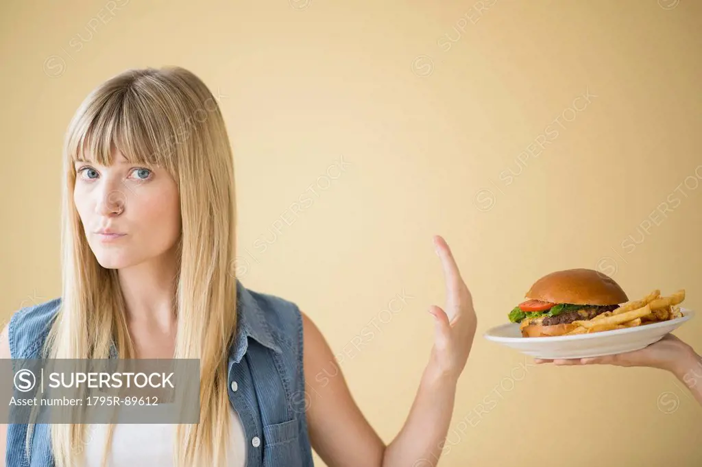 Portrait of woman rejecting hamburger that is being offered to her