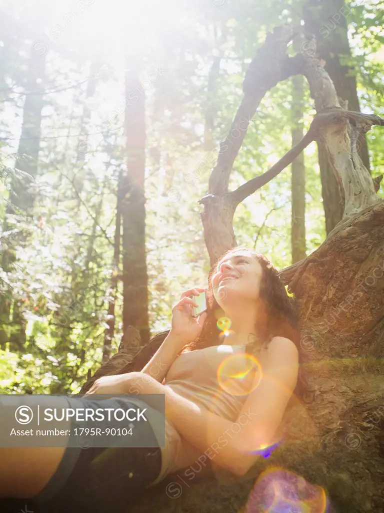 Young woman sitting on log and using cell phone