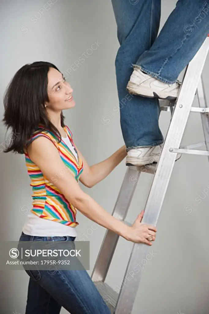 Woman holding ladder while man climbs