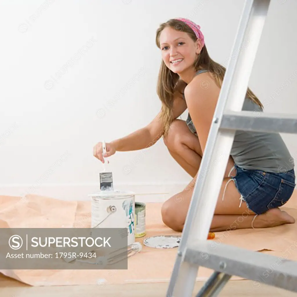 Young woman on tarp with paintbrush and paint can