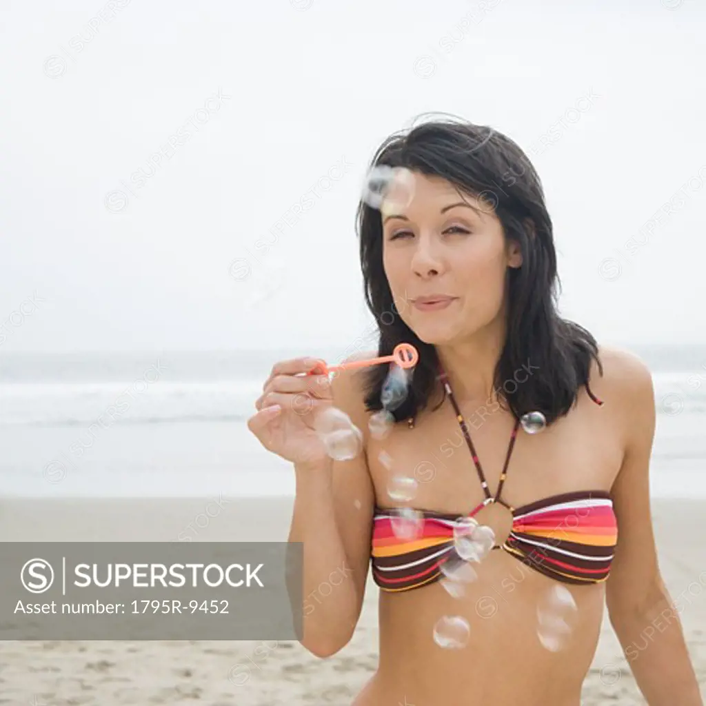 Woman in bikini blowing bubbles at beach