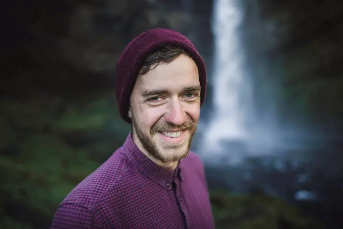 Portrait of smiling young man by Kvernufoss waterfall in Iceland