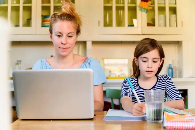 Woman working on laptop and girl (6-7) doing homework