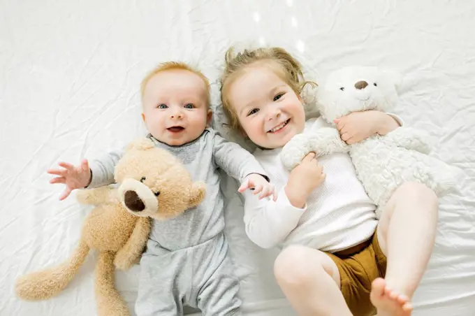 Portrait of siblings lying on bed with their teddy bears