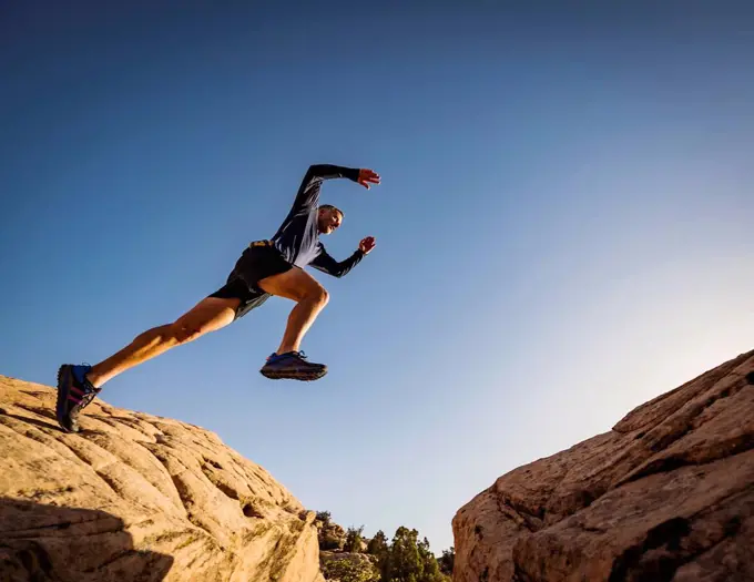 USA, Utah, St. George, Man jumping over rocks while running in eroded landscape