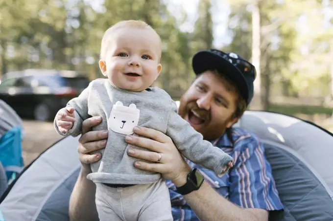 Smiling man holding baby son (6-11 months) on camping, Wasatch-Cache National Forest