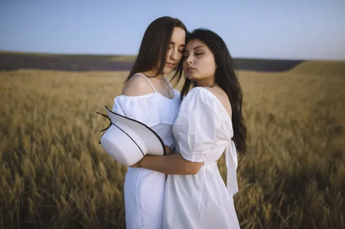 France, Women in white dresses embracing in field