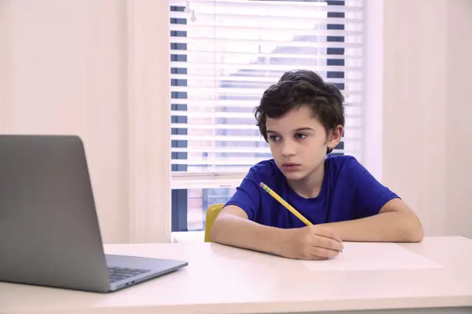 Boy (8-9) sitting at desk at home during remote lesson