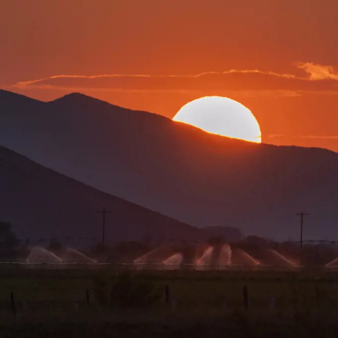 USA, Idaho, Bellevue, Irrigation equipment in field and sun setting behind mountain
