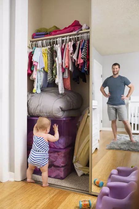 Mid adult man watching baby daughter search box in wardrobe