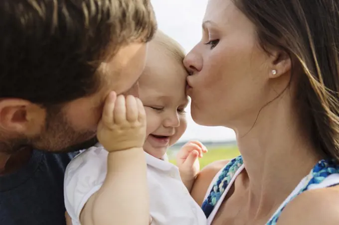 Close-up of mid adult parents kissing baby daughter