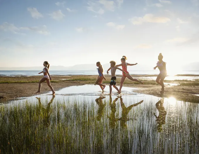 Group of children (10-11, 12-13, 14-15) walking on stepping stones in lake at sunrise