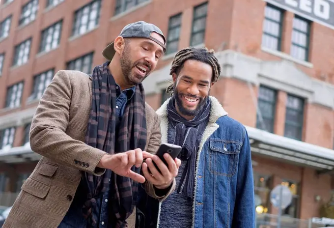 Smiley homosexual couple looking at smart phone in street