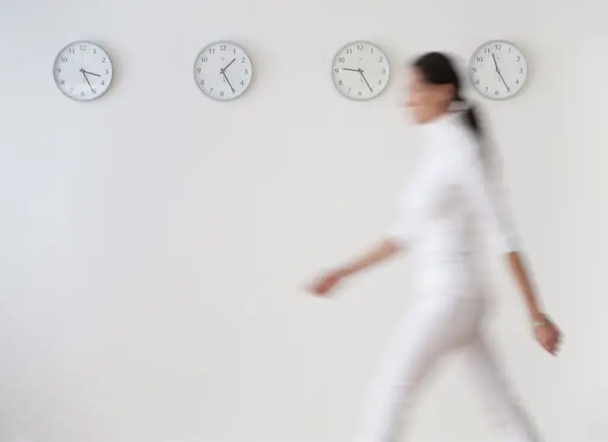Business woman walking along wall with clocks, blurred motion