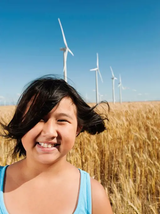 USA, Oregon, Wasco, Cheerful girl 10_11 standing in wheat field with wind turbines in background