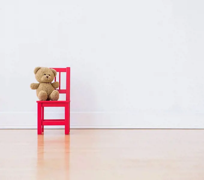 Studio shot of teddy bear sitting on red chair