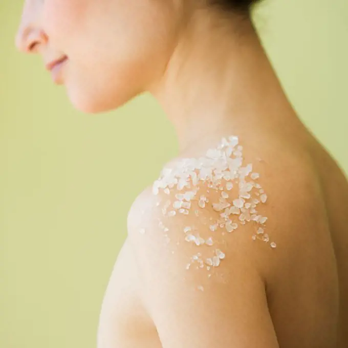 Nude woman with spa salt treatment on shoulder