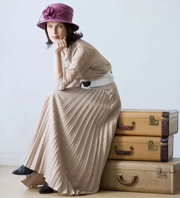 Woman in vintage clothing sitting on suitcases