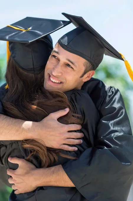 Male and female students embracing on graduation ceremony