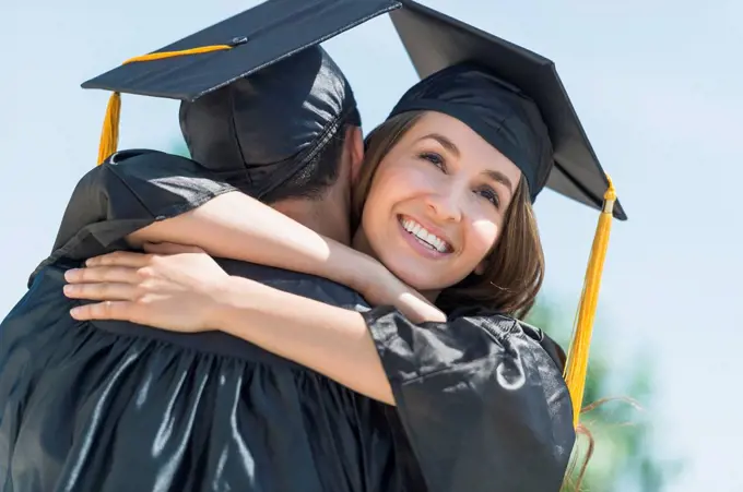 Female and male students embracing on graduation ceremony