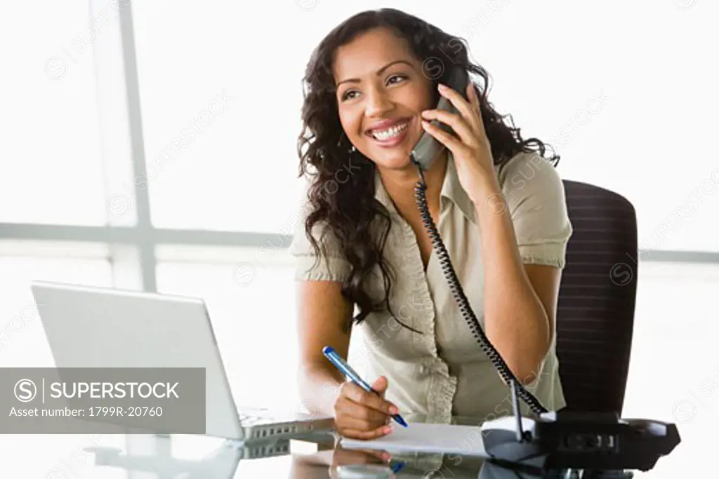 Businesswoman in office on telephone by laptop smiling (high key/selective focus)