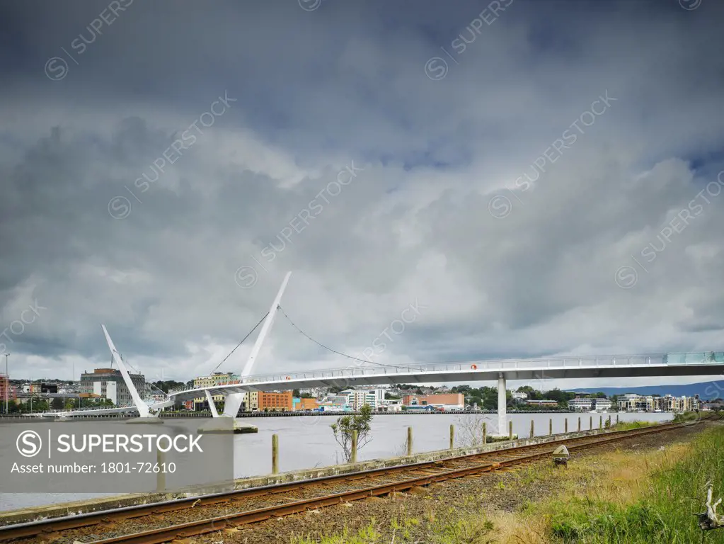 Peace Bridge, Derry, United Kingdom. Architect Wilkinson Eyre Architects, 2011. View from Waterside showing city in background with train tracks.
