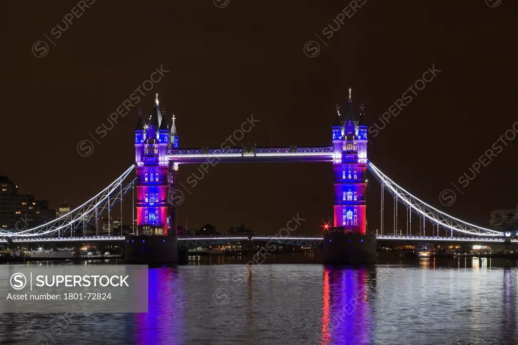 Tower Bridge Re-lighting, London, United Kingdom. Architect Horace Jones, 2012. View of Tower Bridge capturing new lighting system from HMS Belfast. Red, White, Blue Lighting Scheme.