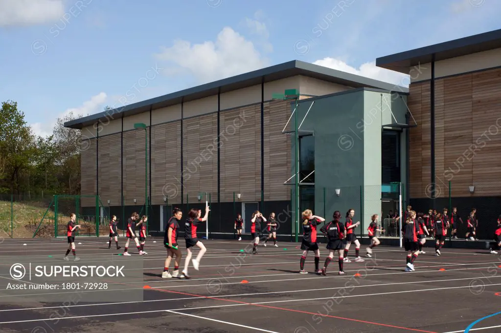 Trinity School Sports Hall, Newbury, United Kingdom. Architect ADP Architects Ltd, 2012. View of south elevation with pupils doing PE on all weather sports pitch.