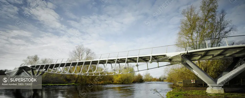 University of Limerick: Living Bridge, Limerick, Ireland. Architect Wilkinson Eyre Architects, 2007. View from riverbank showing bridge in context with river and surrounding landscape.