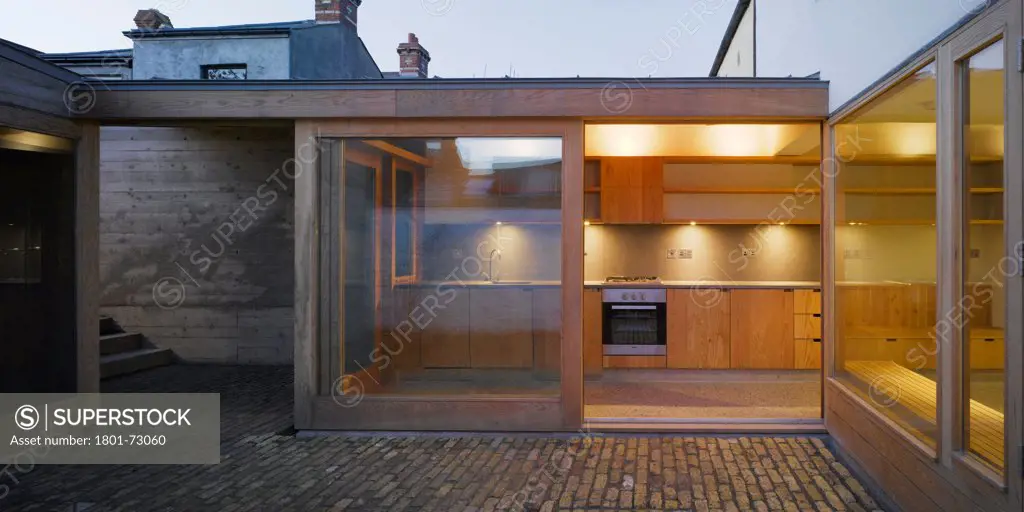 Laneway Wall Garden House, Portobello, Ireland. Architect Donaghy + Dimond, 2011. View from courtyard showing steps and door opened with view to kitchen and interior lighting at dusk.