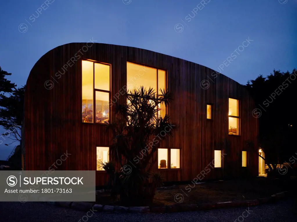 Ballynoe, Dublin, Ireland. Architect McCullough Mulvin, 2006. View of house from driveway showing surrounding landscape and interior lighting at dusk.