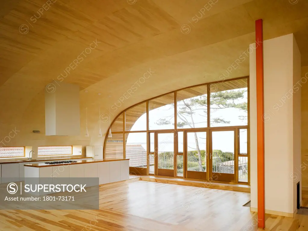 Ballynoe, Dublin, Ireland. Architect McCullough Mulvin, 2006. View of living space showing kitchen, chimney, supporting column, birch plywood lined floor and ceiling and view to exterior.