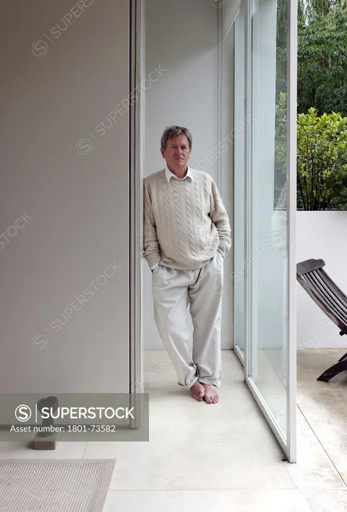 John Pawson at home, Portrait, Europe, United Kingdom,2010, John Pawson. Portrait of Architect John Pawson; full length environmental of John in his house with partial view of garden through floor to ceiling glass sliding door.