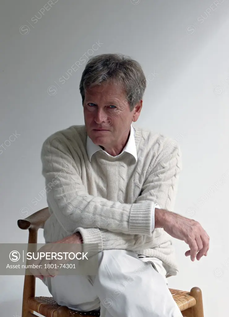 John Pawson at home, London, United Kingdom. Architect: John Pawson, 2010. Portrait of John Pawson sitting on a chair with arms crossed and leaning forward towards camera.