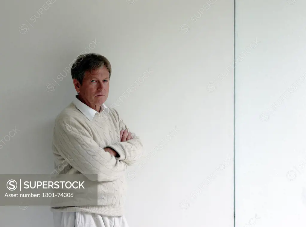 John Pawson at home, London, United Kingdom. Architect: John Pawson, 2010. Portrait of John Pawson standing against a wall in his kitchen/dinning area with arms folded. 3/4 length shot.