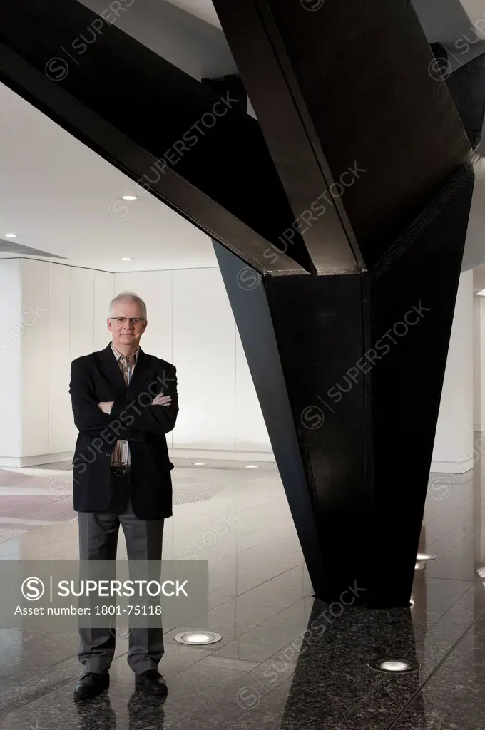 Ken Shuttleworth at 55 Baker Street, London, United Kingdom. Architect: Make Ltd, 2008. General view at reception area looking into lens with smile and arms crossed next to steel supporting column.
