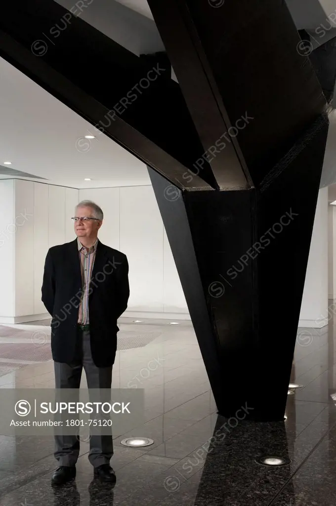 Ken Shuttleworth at 55 Baker Street, London, United Kingdom. Architect: Make Ltd, 2008. General view at reception area looking away with smile and arms behind back next to steel supporting column.
