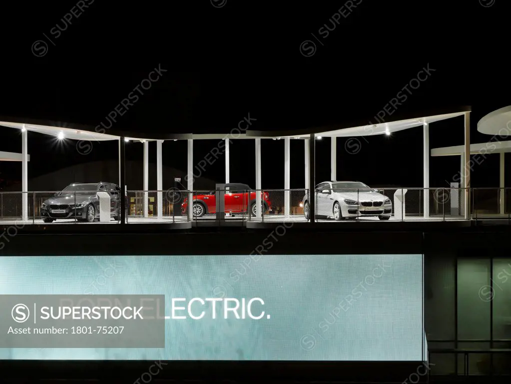BMW Group Pavilion London 2012, London, United Kingdom. Architect: Serie Architects, 2012. Night shot of structure with cars and graphics 'Born Electric'.