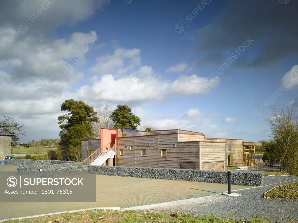 Ballybay Wetland Centre, Ballybay, Ireland. Architect: Solearth Ecological Architecture, 2008. View of building showing stone wire mesh wall, timber cladding and surrounding landscape.