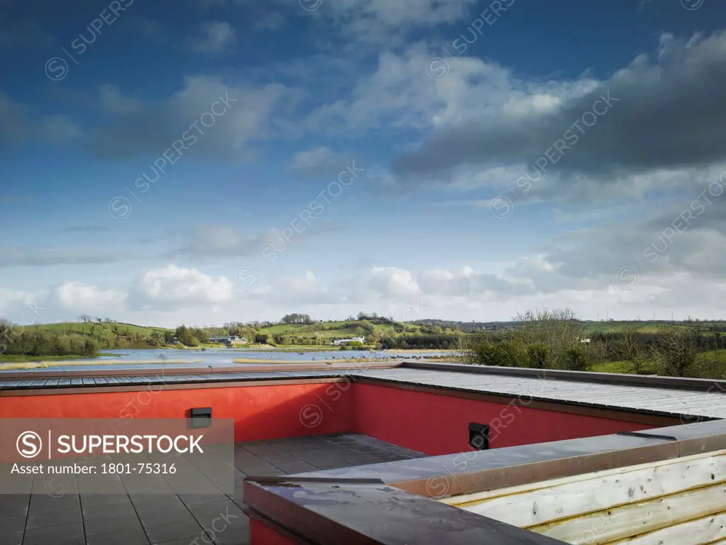 Ballybay Wetland Centre, Ballybay, Ireland. Architect: Solearth Ecological Architecture, 2008. View of roof terrace showing red painted parapet, timber cladding and surrounding landscape.