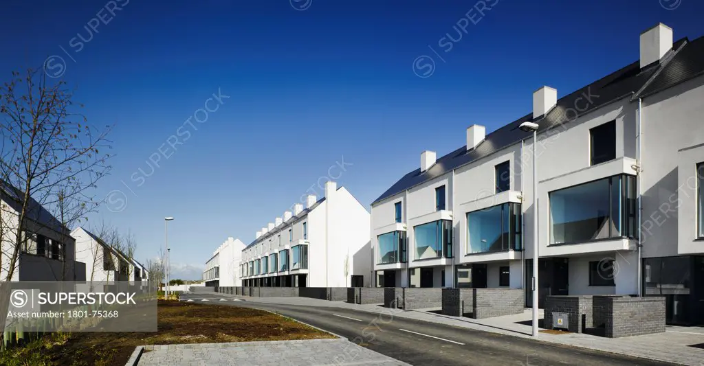 Gleann Bhan, Galway, Ireland. Architect: DTA Architects, 2008. View of road through development showing housing terraces and trees.