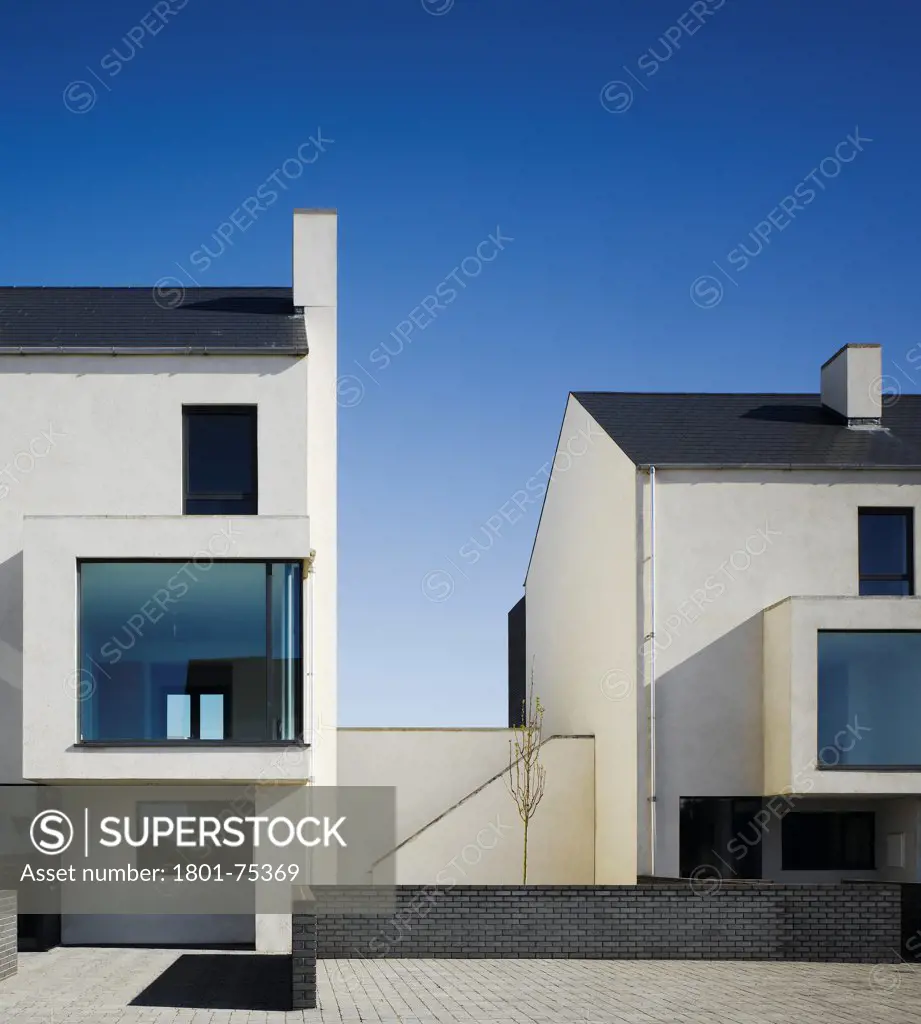 Gleann Bhan, Galway, Ireland. Architect: DTA Architects, 2008. View of space between two terraces showing front elevation and brick wall.