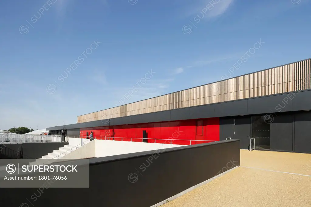 Eton Manor Olympic Park, London, United Kingdom. Architect: Stanton Williams, 2012. Lateral perspective of timber and metal clad structure with signal red access doors.