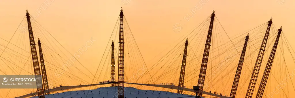 'Up at the O2'- High level walkway over the Millenium Dome, London, United Kingdom. Architect: Rogers Stirk Harbour + Partners, 2012. Distant Panoramic view at dusk with silhouetted figures.