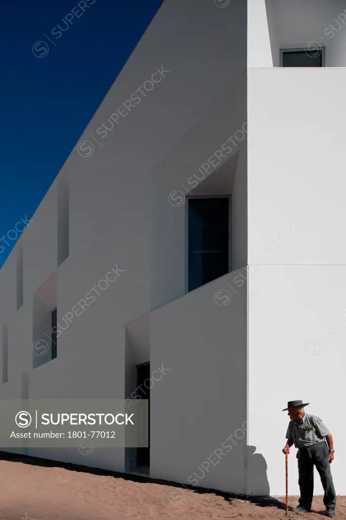 House for Elderly People, Alcaçer do Sal, Portugal. Architect: Francisco Aires Mateus Arquitectos, 2011. View of social housing complex in daylight with man in hat.